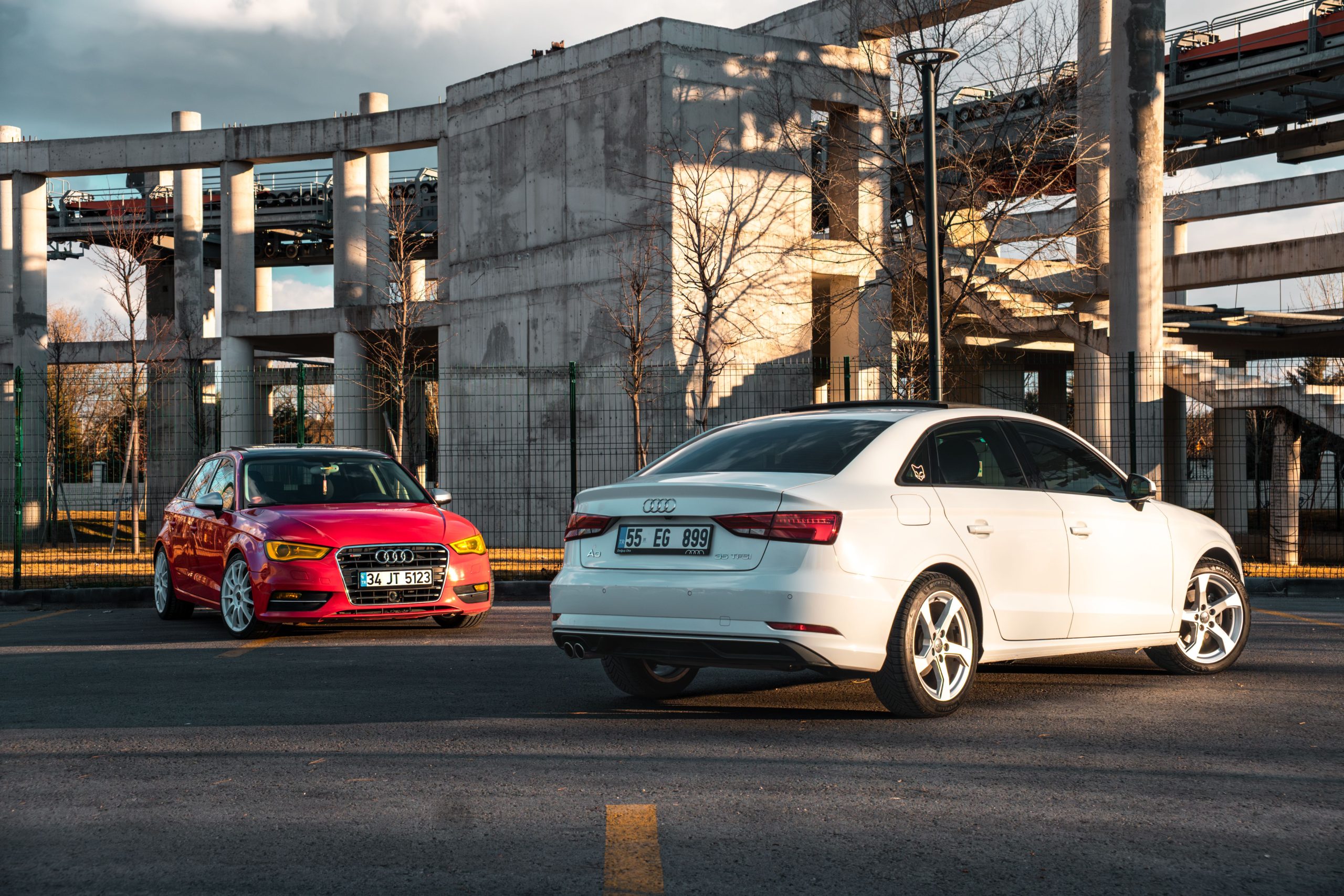 White and red Audi cars parked against industrial architecture outdoors.